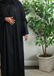 Load image into Gallery viewer, Image of a model wearing a classic black open abaya. The abaya can be styled open or closed, making it versatile for any occasion. It&#39;s perfect for all seasons and can be easily dressed up or down for a chic look
