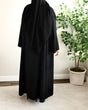 Load image into Gallery viewer, Image of a model wearing a classic black open abaya. The abaya can be styled open or closed, making it versatile for any occasion. It&#39;s perfect for all seasons and can be easily dressed up or down for a chic look
