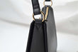 Load image into Gallery viewer, Close shot image of a black shoulder bag, black leather bag with circle gold hardware with zipper 
